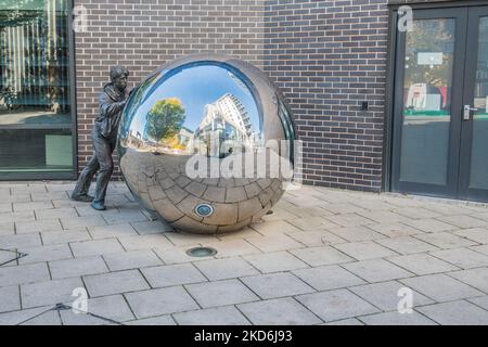 Scultura in , area di Leeds Dock, che mostra una delle due figure in bronzo a grandezza naturale che spingono una sfera a specchio in acciaio inossidabile. Foto Stock