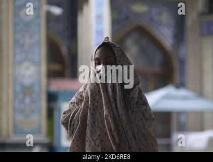 Una donna iraniana velata in chador bianco (codice di abbigliamento islamico) con maschera protettiva prega in un santuario sacro nel nord di Teheran alla fine del primo giorno del mese santo di Ramadan due anni dopo l'epidemia di COVID-19 in Iran, il 3 aprile 2022. (Foto di Morteza Nikoubazl/NurPhoto) Foto Stock