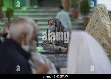 Una donna velata iraniana in chador bianco (codice di abbigliamento islamico) Indossando una maschera protettiva si guarda mentre si trova accanto alle tombe della guerra Iran-Iraq (1980-88) martiri sconosciuti in un santuario santo nel nord di Teheran alla fine del primo giorno del mese santo di Ramadan due anni dopo l'epidemia di COVID-19 in Iran, il 3 aprile 2022. (Foto di Morteza Nikoubazl/NurPhoto) Foto Stock