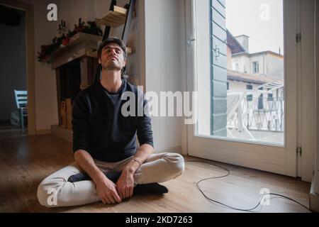 Giovane seduto sul pavimento in meditazione con gambe e braccia incrociate. Foto Stock