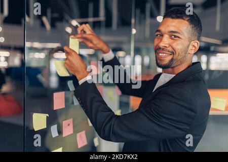 L'uomo d'affari sta attaccando i biglietti appiccicosi sul bordo di affari nell'ufficio moderno Foto Stock