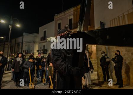Il primo crocifisso in processione con una croce pesante sulle spalle a Noicattaro il 14 aprile 2022. A Noicattaro, la sera del Giovedì Santo, si svolge uno dei più antichi riti della settimana Santa in Puglia: La processione dei Crociferi. I crociferi sono uomini vestiti di abiti neri, cappe tirate giù sul volto e corona di spine sulla testa che, dalla chiesa della Madonna della lama, passeggia a piedi nudi per le strade del centro per visitare gli altari della riposizione allestita nelle chiese della città. Dopo che il falò è acceso, i crogioli si muovono in processione seguita da Tor Foto Stock