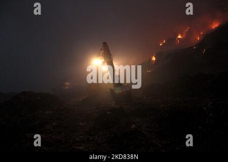 Un escavatore disperde la spazzatura per controllare il fuoco che inghiottisce il sito di discarica di Ghazipur a Nuova Delhi, India il 20 aprile 2022. (Foto di Mayank Makhija/NurPhoto) Foto Stock