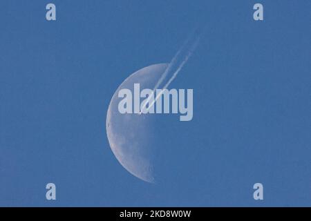 Un aereo passeggeri sta navigando a 40,000 piedi di altitudine e passando di fronte alla mezza luna, in una giornata di primavera senza nuvole, mentre l'aereo vola sopra l'Europa nel cielo olandese. Moonpass è l'obiettivo ultimo dei fotografi di aviazione, i planespoter. Durante il volo, il jet del passeggero lascia dietro contraglie o tracce di condensazione, una linea di vapore bianca che passa davanti al satellite naturale della Terra e all'oggetto celeste più vicino nell'universo. Eindhoven, Paesi Bassi il 24 aprile 2022. (Foto di Nicolas Economou/NurPhoto) Foto Stock