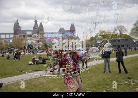 Un uomo crea bolle di sapone nel parco. I Paesi Bassi festeggiano il King's Day dopo due anni di cancellazione a causa della pandemia di Coronavirus COVID-19 e delle restrizioni e misure di blocco. Migliaia di abitanti del luogo, festeggiatori e visitatori hanno visitato il centro della città, i parchi vicino al Rijksmuseum, i canali di Amsterdam per celebrare con varie feste il compleanno del re Willem-Alexander conosciuto come Koningsdag, una festa nazionale olandese. Tutti i tipi di barche e navi sono visti nei canali che passano sotto i famosi ponti e vicino alle case strette di Amsterdam con la gente sul ballo e hav Foto Stock