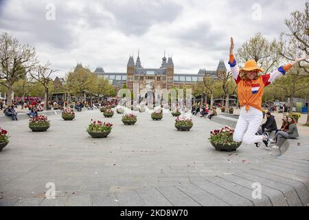 Una signora degli Stati Uniti, un turista, salta davanti al Rijksmuseum indossando abiti arancioni con la bandiera olandese. I Paesi Bassi festeggiano il King's Day dopo due anni di cancellazione a causa della pandemia di Coronavirus COVID-19 e delle restrizioni e misure di blocco. Migliaia di abitanti del luogo, festeggiatori e visitatori hanno visitato il centro della città, i parchi vicino al Rijksmuseum, i canali di Amsterdam per celebrare con varie feste il compleanno del re Willem-Alexander conosciuto come Koningsdag, una festa nazionale olandese. Tutti i tipi di barche e imbarcazioni sono visibili nei canali che passano sotto il famoso ponte Foto Stock