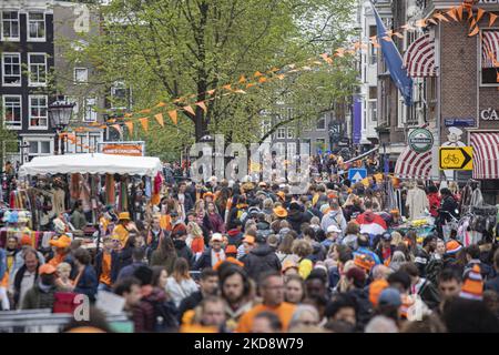 Folle di persone che indossano principalmente abiti arancioni e che hanno la bandiera olandese come si vede nelle strade di Amsterdam, mentre i Paesi Bassi celebra il giorno del Re dopo due anni di cancellazione a causa della pandemia di Coronavirus COVID-19 e le restrizioni e misure di blocco. Migliaia di abitanti del luogo, festeggiatori e visitatori hanno visitato il centro della città, i parchi vicino al Rijksmuseum, i canali di Amsterdam per celebrare con varie feste il compleanno del re Willem-Alexander conosciuto come Koningsdag, una festa nazionale olandese. Tutti i tipi di barche e imbarcazioni sono visibili nei canali che passano sotto i famosi ponti Foto Stock