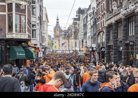 Folle di persone che indossano principalmente abiti arancioni e che hanno la bandiera olandese come si vede nelle strade di Amsterdam, mentre i Paesi Bassi celebra il giorno del Re dopo due anni di cancellazione a causa della pandemia di Coronavirus COVID-19 e le restrizioni e misure di blocco. Migliaia di abitanti del luogo, festeggiatori e visitatori hanno visitato il centro della città, i parchi vicino al Rijksmuseum, i canali di Amsterdam per celebrare con varie feste il compleanno del re Willem-Alexander conosciuto come Koningsdag, una festa nazionale olandese. Tutti i tipi di barche e imbarcazioni sono visibili nei canali che passano sotto i famosi ponti Foto Stock