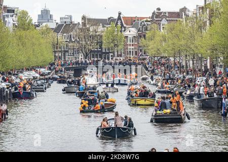 I Paesi Bassi festeggiano il King's Day dopo due anni di cancellazione a causa della pandemia di Coronavirus COVID-19 e delle restrizioni e misure di blocco. Migliaia di abitanti del luogo, festeggiatori e visitatori hanno visitato il centro della città, i parchi vicino al Rijksmuseum, i canali di Amsterdam per celebrare con varie feste il compleanno del re Willem-Alexander conosciuto come Koningsdag, una festa nazionale olandese. Tutti i tipi di barche e navi sono visti nei canali che passano sotto i famosi ponti e vicino alle case strette di Amsterdam con persone che ballano e divertirsi. Le barche sfilano giù nel dentro Foto Stock