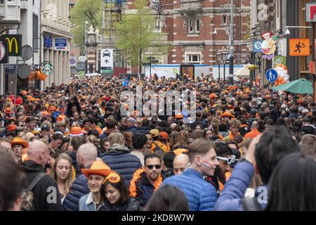 Folle di persone che indossano principalmente abiti arancioni e che hanno la bandiera olandese come si vede nelle strade di Amsterdam, mentre i Paesi Bassi celebra il giorno del Re dopo due anni di cancellazione a causa della pandemia di Coronavirus COVID-19 e le restrizioni e misure di blocco. Migliaia di abitanti del luogo, festeggiatori e visitatori hanno visitato il centro della città, i parchi vicino al Rijksmuseum, i canali di Amsterdam per celebrare con varie feste il compleanno del re Willem-Alexander conosciuto come Koningsdag, una festa nazionale olandese. Tutti i tipi di barche e imbarcazioni sono visibili nei canali che passano sotto i famosi ponti Foto Stock