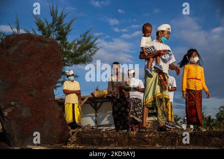 I devoti indù balinesi si riuniscono mentre eseguono preghiere durante il Melasti, una cerimonia di purificazione davanti a Nyepi in una spiaggia a Bali, Indonesia, il 1 marzo 2022. Gli indù balinesi vestiti in abiti prevalentemente bianchi trasportavano sacre effigi di dei e dee e paraphernalia rituali dai loro templi del villaggio alla spiaggia per eseguire una cerimonia di purificazione chiamata rituale Melasti. Gli indù balinesi credono che il rituale Melasti sia un must che si esibisce prima del giorno del Nyepi, il giorno del silenzio, per purificare l'anima e la natura, ricaricare il potere soprannaturale degli oggetti sacri del tempio e pulire il sistema Foto Stock