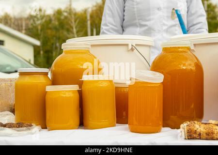 Vasetti di vetro di diverse dimensioni, ripieni di miele di api mature di colore giallo chiaro di Bashkir. Vi è commercio alla fiera agricola autunnale. Foto Stock