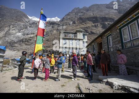 Alunni, scolari come si vede fuori della scuola locale sotto la vetta di Langtang Lirung. La cima di Langtang Lirung come visto dal villaggio di Langtang, parte della montagna di Langtang Himal in Nepal con il punto più alto all'altezza di 7234m o 23734 piedi. Langtang Lirung è la montagna 99th più alta del mondo e la cima è stata raggiunta per la prima volta nel 1978. Il 25 aprile 2015, un massiccio terremoto di magnitudo 7,8 ha provocato una valanga e una frana nel villaggio di Langtang che ha ucciso direttamente 243 persone e svanito il villaggio. Il Parco Nazionale di Langtang è una meta popolare per il trekking e il viaggio Foto Stock