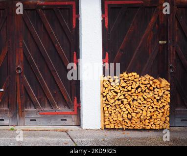 Una pila di tronchi di legna da ardere tagliato di recente sul terreno di fronte ad una porta di legno all'aperto Foto Stock