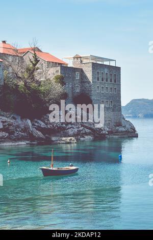 Piccola barca da pesca sul mare Adriatico vicino all'isola Sveti Stefan, Montenegro. Turquiose acqua, isolotto con edifici storici. Montagne nel Foto Stock
