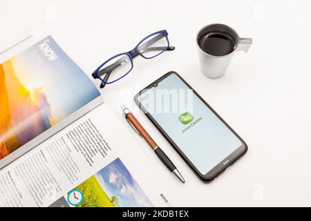 In questa illustrazione, il 27 maggio 2022, un logo John Deere appare sullo schermo di uno smartphone su una scrivania accanto a un bar, una penna, occhiali e una rivista ad Atene, in Grecia. (Foto Illustrazione di Nikolas Kokovlis/NurPhoto) Foto Stock