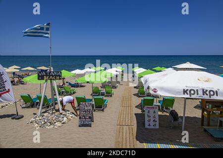 Turismo in Grecia. La costa della città di Rethymno con la lunga spiaggia sabbiosa e i bar sulla spiaggia dell'isola di Creta con le montagne sullo sfondo. Le persone si abbronzano indossando costume da bagno, costume da bagno, bikini, godendosi il sole sotto l'ombrellone al bar sulla spiaggia su un lettino e nuotando nel mare cristallino. Rethymno è una storica città balneare mediterranea sulla costa settentrionale di Creta, adagiato sul Mar Egeo con una popolazione di 40,000 persone. Una destinazione turistica con un porto storico veneziano e città, siti archeologici, spiagge sabbiose infinite, sport acquatici, bella t Foto Stock