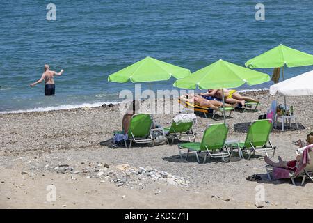 Turismo in Grecia. La costa della città di Rethymno con la lunga spiaggia sabbiosa e i bar sulla spiaggia dell'isola di Creta con le montagne sullo sfondo. Le persone si abbronzano indossando costume da bagno, costume da bagno, bikini, godendosi il sole sotto l'ombrellone al bar sulla spiaggia su un lettino e nuotando nel mare cristallino. Rethymno è una storica città balneare mediterranea sulla costa settentrionale di Creta, adagiato sul Mar Egeo con una popolazione di 40,000 persone. Una destinazione turistica con un porto storico veneziano e città, siti archeologici, spiagge sabbiose infinite, sport acquatici, bella t Foto Stock