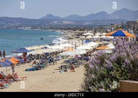 Turismo in Grecia. La costa della città di Rethymno con la lunga spiaggia sabbiosa e i bar sulla spiaggia dell'isola di Creta con le montagne sullo sfondo. Le persone si abbronzano indossando costume da bagno, costume da bagno, bikini, godendosi il sole sotto l'ombrellone al bar sulla spiaggia su un lettino e nuotando nel mare cristallino. Rethymno è una storica città balneare mediterranea sulla costa settentrionale di Creta, adagiato sul Mar Egeo con una popolazione di 40,000 persone. Una destinazione turistica con un porto storico veneziano e città, siti archeologici, spiagge sabbiose infinite, sport acquatici, bella t Foto Stock