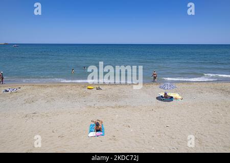 Turismo in Grecia. La costa della città di Rethymno con la lunga spiaggia sabbiosa e i bar sulla spiaggia dell'isola di Creta con le montagne sullo sfondo. Le persone si abbronzano indossando costume da bagno, costume da bagno, bikini, godendosi il sole sotto l'ombrellone al bar sulla spiaggia su un lettino e nuotando nel mare cristallino. Rethymno è una storica città balneare mediterranea sulla costa settentrionale di Creta, adagiato sul Mar Egeo con una popolazione di 40,000 persone. Una destinazione turistica con un porto storico veneziano e città, siti archeologici, spiagge sabbiose infinite, sport acquatici, bella t Foto Stock