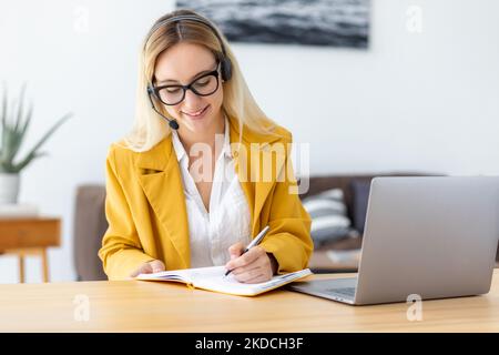 Una giovane donna sostiene un lavoratore o un agente, prendendo appunti in un notebook che lavora in remoto, consulta un cliente Foto Stock