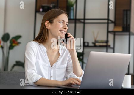 Giovane donna d'affari che lavora nell'ufficio moderno mentre parla al telefono Foto Stock