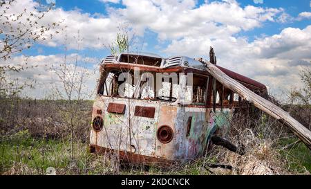 Un vecchio autobus abbandonato si trova arrugginito nelle erbacce di un campo rurale sotto un cielo nuvoloso Foto Stock