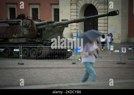 Una donna con un ombrello passa accanto a un carro armato russo Howitzer vicino al Castello reale di Varsavia, Polonia, il 28 giugno 2022. Due carri armati dell'esercito russo distrutti sono in mostra sulla Piazza del Castello nella Città Vecchia dopo essere stati trasportati dall'Ucraina. Uno dei carri armati, un T-72 è stato distrutto nel distretto di Buka vicino a Kyiv, dove a marzo l'esercito russo ha commesso esecuzioni di massa di civili. Il secondo serbatoio in esposizione è un Howitzer semovente 2S19 Msta del peso di circa 42 mila chili. (Foto di Str/NurPhoto) Foto Stock