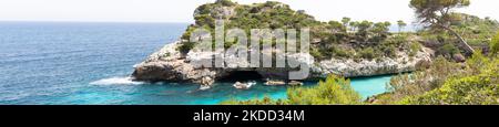 Una foto panoramica della baia di es calo des Moro Beach, nel sud di Maiorca, con una formazione rocciosa coperta di alberi e un mare blu scuro sullo sfondo Foto Stock