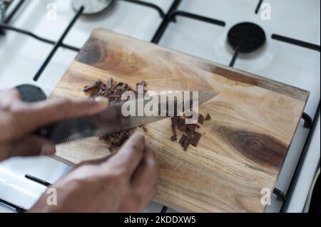 Cucinare con il cioccolato come cuoco usa un grande coltello affilato per tritare una barretta di caramelle al cioccolato su un tagliere di legno Foto Stock