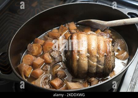 Cottura in casseruola di manzo in una pentola di metallo con carne arrotolata circondata da verdure fresche e sugo in agitazione con un cucchiaio di legno Foto Stock