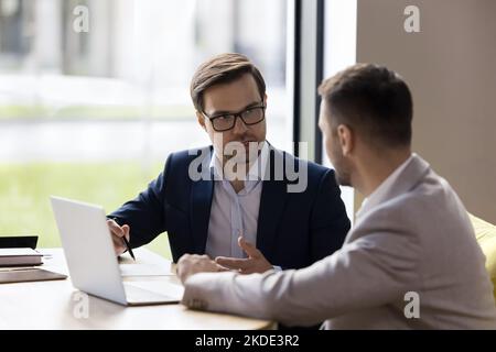 Due colleghi discutono del lavoro di squadra, lavorando insieme al notebook in ufficio Foto Stock