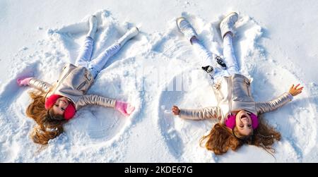 Angeli d'inverno. Le ragazze felici dei capretti su fanno le ali dell'angelo della neve. Due bambini che fanno angelo di neve, sdraiati sulla neve. Bambino eccitato che gioca su sfondo invernale Foto Stock