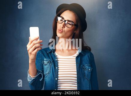 Festeggia te stesso con un selfie. Foto studio di una bella giovane donna che prende un selfie su uno sfondo blu. Foto Stock