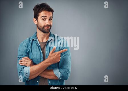 Indirizza la tua attenzione qui...Studio girato di un bel giovane uomo che indica lo spazio delle copie su uno sfondo grigio. Foto Stock