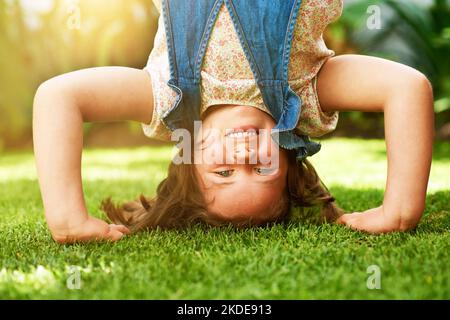Posso stare in piedi sulle mie mani. Ritratto di una bambina felice che fa un cavalletto sull'erba fuori. Foto Stock