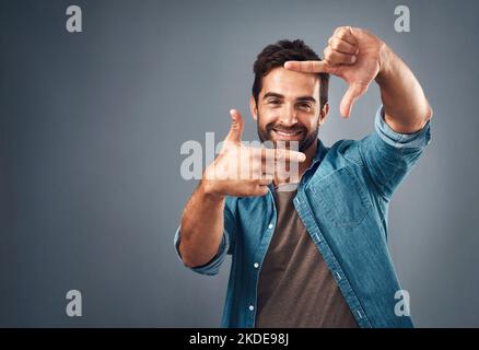 Fantastico devo solo scattare la tua foto. Studio ritratto di un bel giovane che fa una cornice dito su uno sfondo grigio. Foto Stock