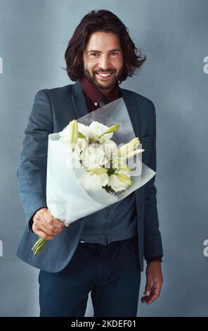 Per il mio amore speciale. Studio shot di un bel giovane vestito elegantemente con un bouquet di fiori su sfondo grigio. Foto Stock