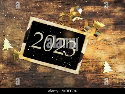 2023 scritto su una piccola tavola nera su sfondo di legno illuminato - biglietto di auguri per il nuovo anno Foto Stock