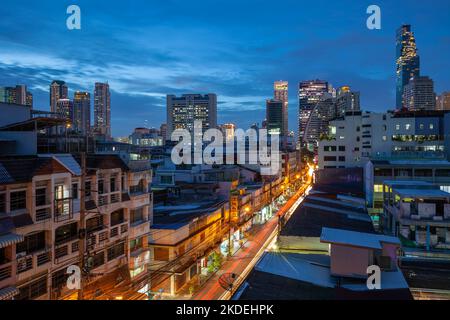 Vista notturna della strada nel quartiere di Sathon, con la torre del re Power Mahanakhon e l'ospedale di Saint Louis sullo sfondo, Bangkok Foto Stock