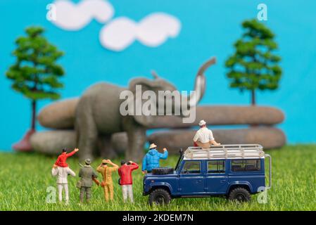 Giocattoli in miniatura di un gruppo di persone in viaggio safari guardando loxodonta elefante africano - un cacciatore, padre e figlio in giro a spalla, fotografo con Foto Stock