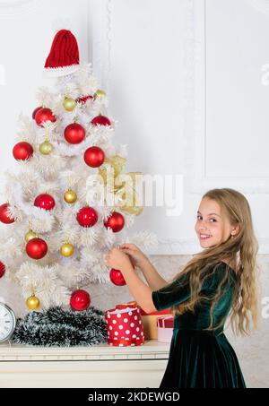 Bambino ha messo la sfera di ornamento di natale sull'albero bianco artificiale. Top natale decorazione idee per la stanza dei bambini. I capretti possono illuminare in su l'albero di natale vicino Foto Stock