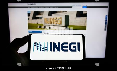 Persona che tiene il cellulare con il logo dell'agenzia di statistiche messicane INEGI sullo schermo di fronte alla pagina web. Messa a fuoco sul display del telefono. Foto Stock