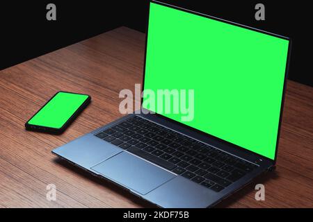 Immagine mockup con schermo verde sul computer e smartphone sulla scrivania in legno. Sfondo per il testo pubblicitario. Spazio per il design. Foto Stock