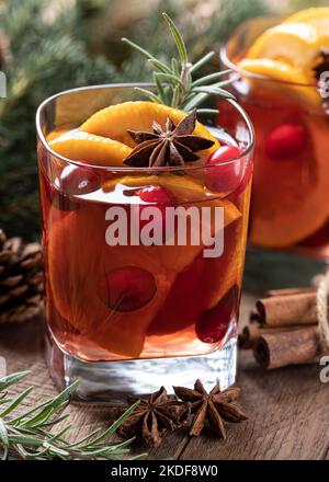 VIN brulé con fettine d'arancia, mirtilli rossi e spezie su un rustico tavolo di legno con decorazione dell'albero di Natale sullo sfondo Foto Stock