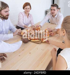 Il team Aziende di mangiare la pizza in ufficio seduti attorno al tavolo Foto Stock