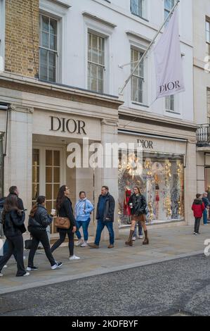 Le persone che si trovano in città per fare shopping passano dal negozio di moda Dior a New Bond Street, Mayfair, Londra, Inghilterra, Regno Unito Foto Stock