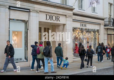 Le persone che si trovano in città per fare shopping passano dal negozio di moda Dior a New Bond Street, Mayfair, Londra, Inghilterra, Regno Unito Foto Stock