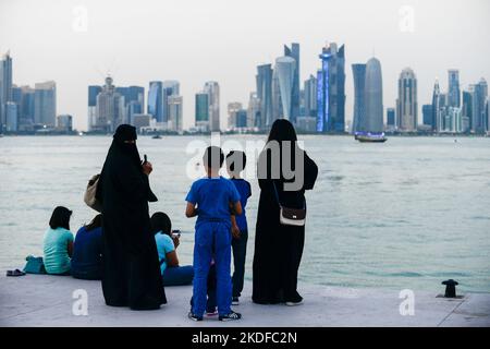 QATAR, Doha, skyline di eastbay con grattacielo, donne qatari in piedi con bambini in cornicione, dietro lavoratori migranti seduti dall'asia Foto Stock