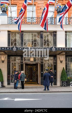 Un gruppo di quattro persone sta in conversazione fuori dall'ingresso principale del Claridge's Hotel su Brook Street, Londra, Inghilterra, Regno Unito Foto Stock